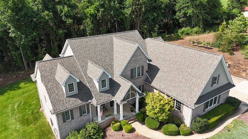Aerial drone view of a finished grey asphalt shingle roof installation on a large brick and stone house.