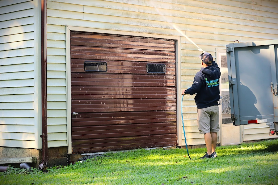 An integrity Roofing worker powerwashing a garage door